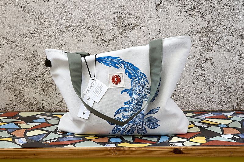 Natural canvas shoulder tote with olive webbing straps, printed with a blue koi curving across the front.