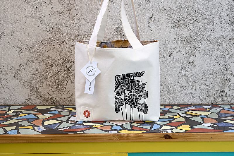 Natural canvas tote printed in black with a cluster of hand-carved wildflowers, patterned lining and the workshop's hang tag.